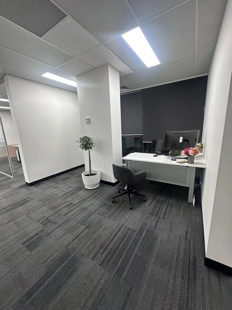 Corner office with a white desk, chair and potted plant on dark carpet