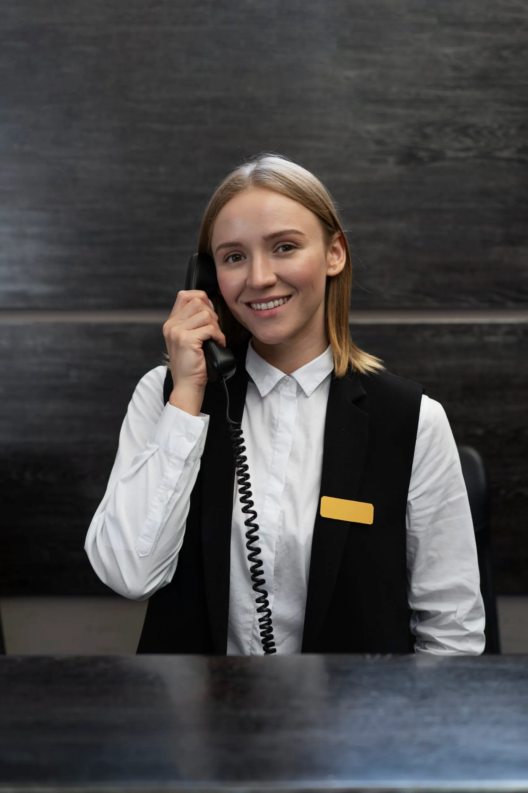 Receptionist in a dark vest answering the telephone at a front desk